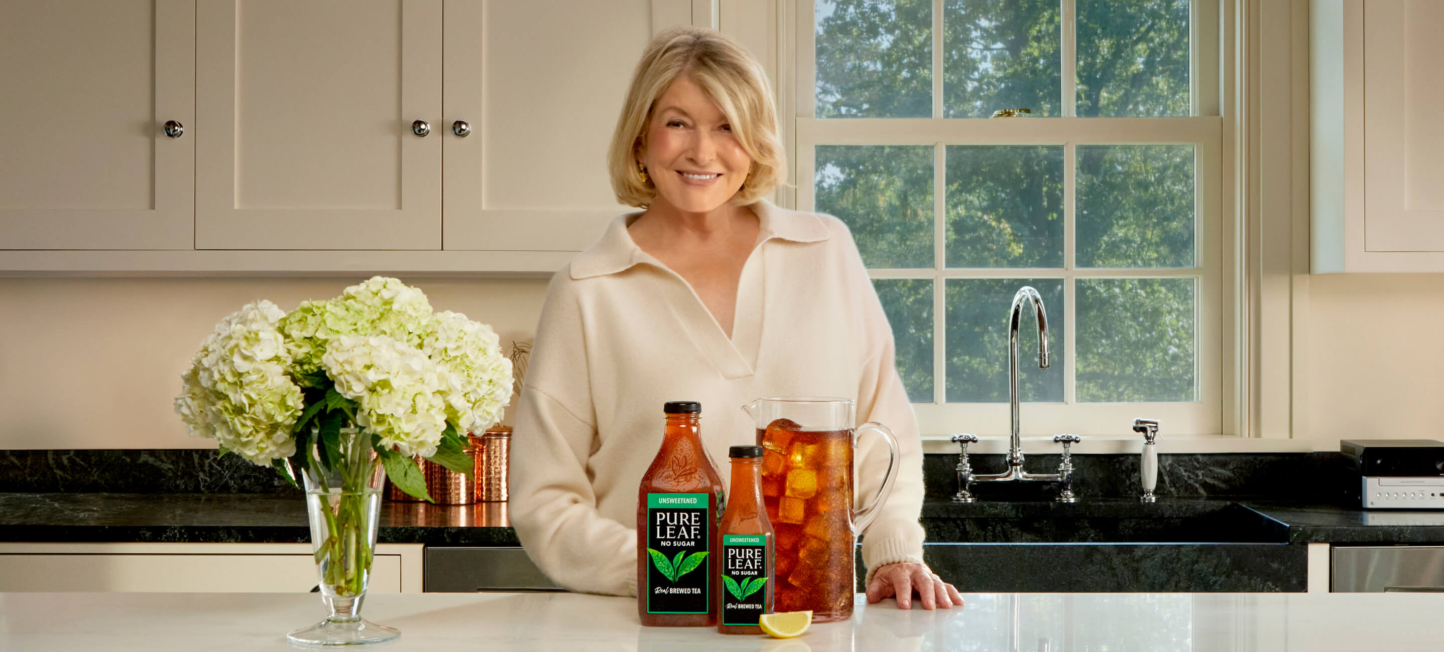 Martha Stewart at a kitchen counter with 2 Pure Leaf bottles and a Pitcher of Pure Leaf Iced Tea.